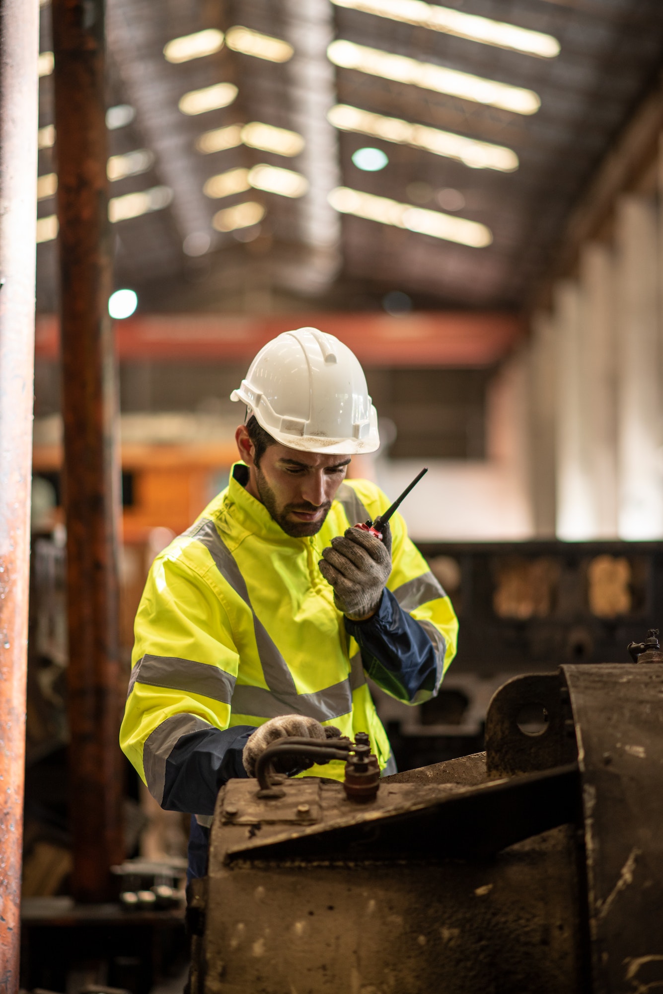 Mature man in high-visibility workwear using a radio on a construction site, inspecting machinery, emphasizing thermal power planning and fuel services.