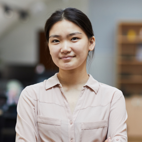 Young woman in a light pink blouse, smiling confidently, in an office setting, representing professionalism and service in the context of BettyJet's fuel delivery solutions.