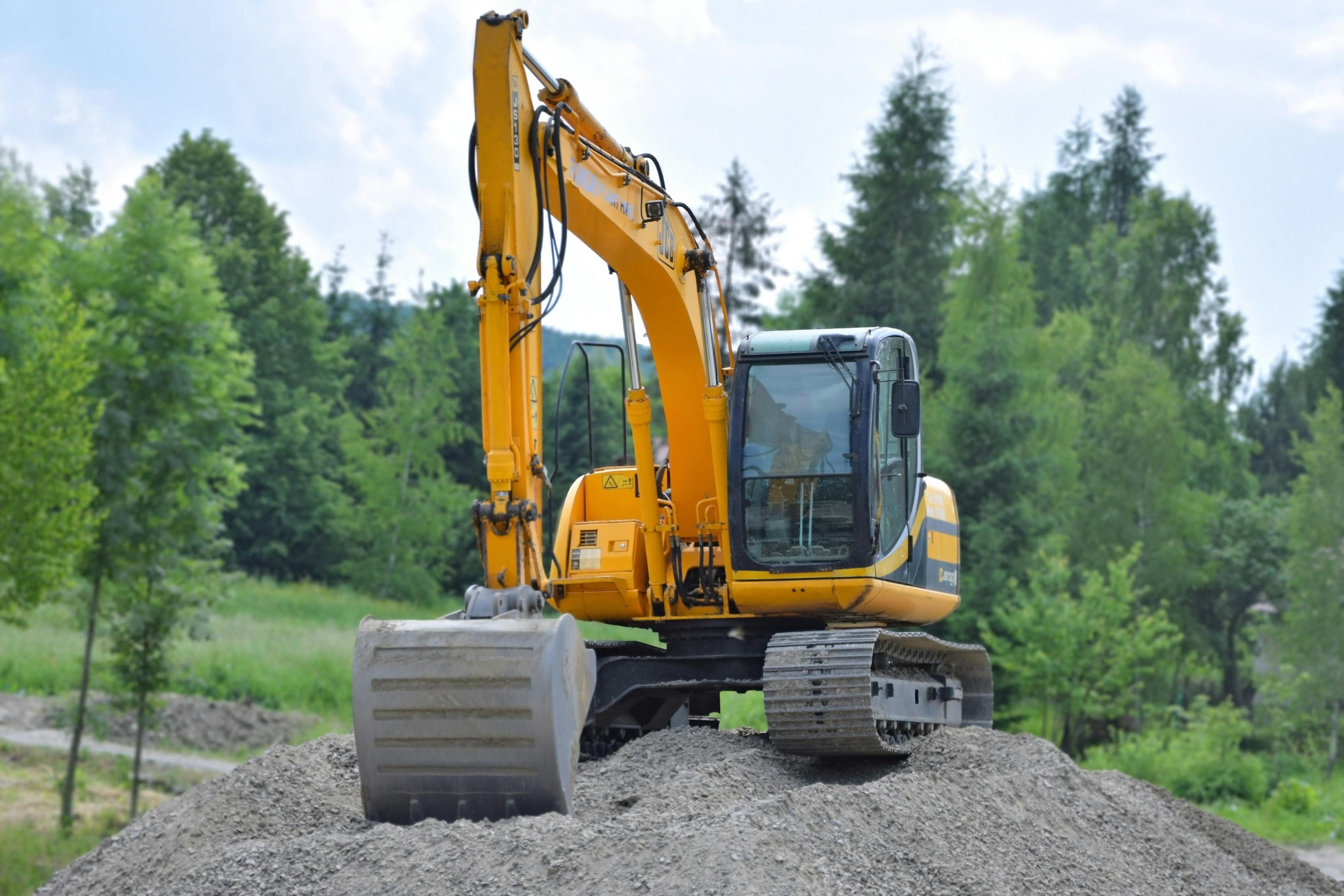 Yellow excavator parked on a gravel mound at a rural job site surrounded by trees, symbolizing heavy equipment operations and on-site diesel fueling for construction crews.